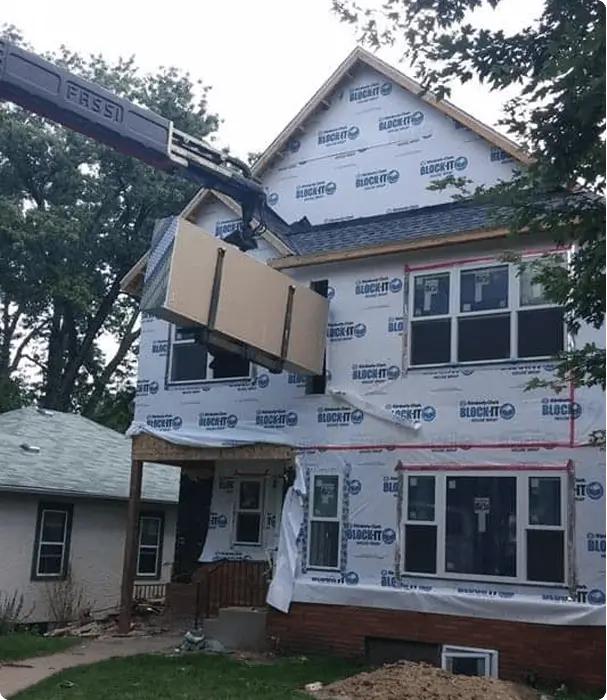 Drywall delivery to residential construction site with crane lifting materials to upper floor
