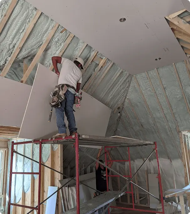 Worker installing drywall on sloped ceiling using scaffolding in residential construction project